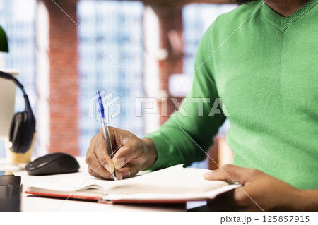Person preparing for school exam, practicing on notepad at home office desk, close up. African american student doing homework, writing down info with pen, researching for college tests Person preparing for school exam, practicing on notepad at home office desk, close up. African american student doing homework, writing down info with pen, researching for college tests 125857915