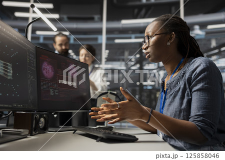 Scared admin in data center panicked by virus alert, initiating protocol to protect critical systems. African American woman in server room assessing compromised gear after hacker attack Scared admin in data center panicked by virus alert, initiating protocol to protect critical systems. African American woman in server room assessing compromised gear after hacker attack 125858046