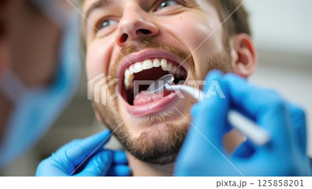 Close-up of Man's Smile During Dental Check-up with Dental Mirror 125858201