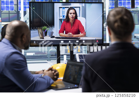 Compliance officer aids shareholders in assessing laws compliance during teleconference meeting. Investors in industrial plant examine financial statements and evaluate assets during online videocall Compliance officer aids shareholders in assessing laws compliance during teleconference meeting. Investors in industrial plant examine financial statements and evaluate assets during online videocall 125858210