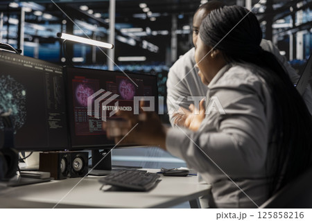 Technicians in data center viewing hacking security breach alert of zero day exploit vulnerability. Cybersecurity colleagues doing brainstorming to trace intrusion origin and apply emergency patches 125858216