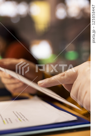 Aged student with a focused expression reading files at college library, academic research and reading textbooks to complete his degree and enrich his understanding of literature. Close up. 125858447