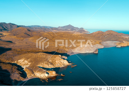 Rocky seashore with clear blue sky. Seascape in the evening. Cabo de Gata-Nijar reserve. Almeria Andalusia Spain Rocky seashore with clear blue sky. Seascape in the evening. Cabo de Gata-Nijar reserve. Almeria Andalusia Spain 125858727