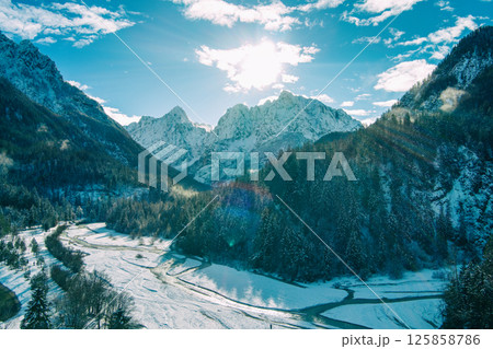 Mountain valley with the river in winter. The tops of the mountains are covered with snow. View of the Alps in Kranjska Gora at sunrise. Triglav national park. Slovenia, Europe Mountain valley with the river in winter. The tops of the mountains are covered with snow. View of the Alps in Kranjska Gora at sunrise. Triglav national park. Slovenia, Europe 125858786