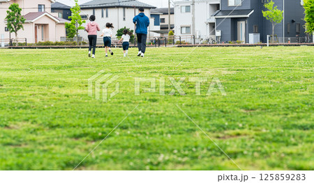 芝生の公園を走る家族の後ろ姿 125859283