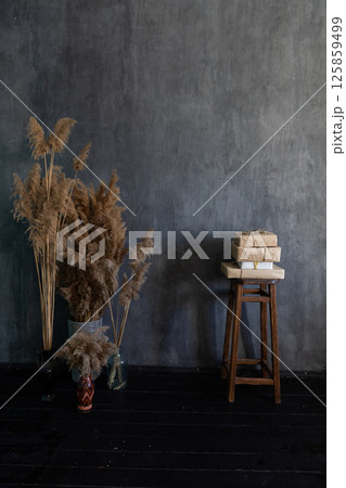 A vase with flowers and a chair with books in the interior of a dark gray room 125859499