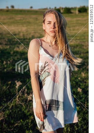 Portrait of a woman in a summer dress on a green field at sunset Portrait of a woman in a summer dress on a green field at sunset 125859512
