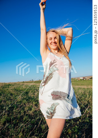 Woman in dress laughing and running on green field at sunset Woman in dress laughing and running on green field at sunset 125859513