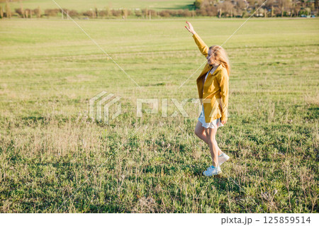 Woman in dress laughing and running on green field at sunset 125859514