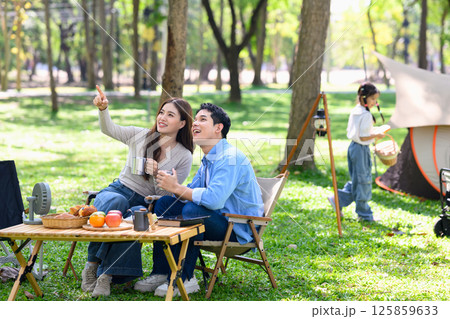 Relaxed family sitting outdoors at a campsite surrounded by trees and fresh greenery Relaxed family sitting outdoors at a campsite surrounded by trees and fresh greenery 125859633
