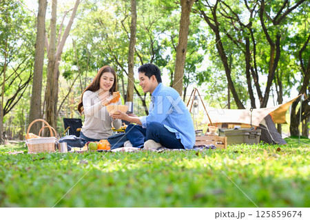 Happy couple enjoying picnic meal together while camping in a forest 125859674