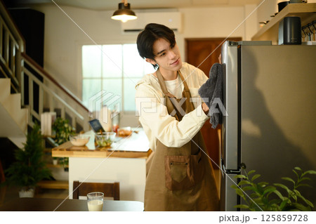 Smiling man doing household chores, cleaning the refrigerator with a cloth 125859728
