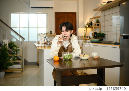 Young man in apron enjoying a healthy breakfast at home Young man in apron enjoying a healthy breakfast at home 125859740