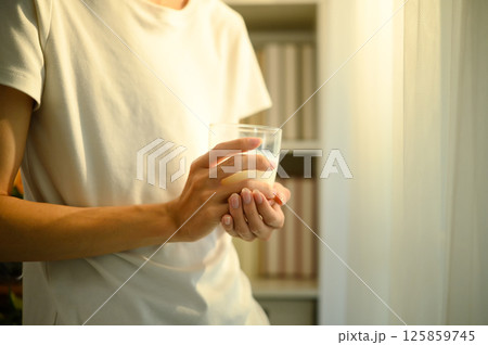 Close up of a man holding a glass of milk while standing indoors in warm natural light Close up of a man holding a glass of milk while standing indoors in warm natural light 125859745