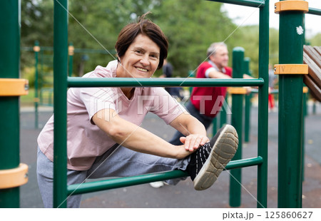 Elderly woman doing stretching exercises on the parallel bars at an outdoor sports ground Elderly woman doing stretching exercises on the parallel bars at an outdoor sports ground 125860627