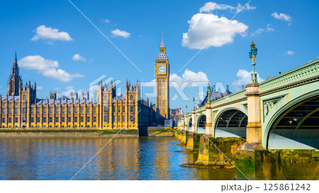 Houses of Parliament and Big Ben rise majestically above the River Thames, with Westminster Bridge creating a picturesque view under a clear blue sky in London. 125861242