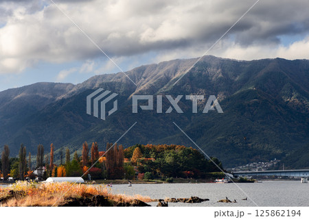 Autumn foliage along the shore of Lake Kawaguchi with colorful trees and mountain slopes Autumn foliage along the shore of Lake Kawaguchi with colorful trees and mountain slopes 125862194