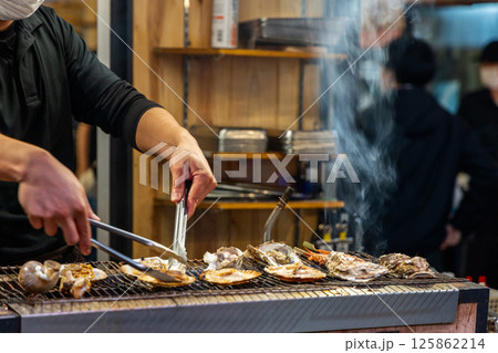 Street food preparation of shellfish on grill in Japan with chef handling fresh oysters and scallops 125862214
