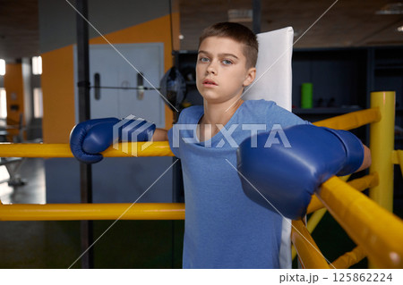 Teenage boy boxer wearing gloves inside boxing ring posing for camera Teenage boy boxer wearing gloves inside boxing ring posing for camera 125862224