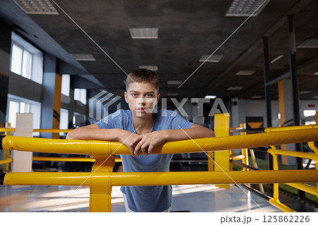 Portrait of tired teenage boy standing in boxing ring at modern gym Portrait of tired teenage boy standing in boxing ring at modern gym 125862226