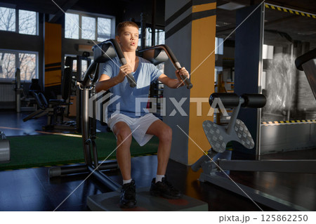Athletic teenage boy enjoying hard training on fitness machine at gym 125862250