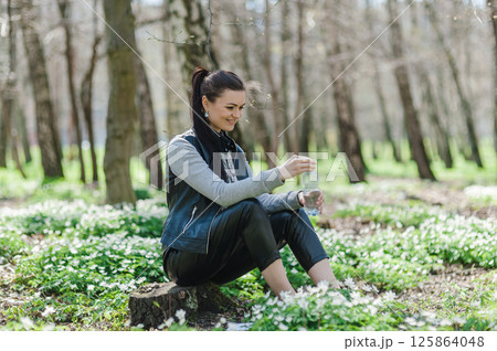 A girl in the park opens a bottle of water. A woman is resting in the forest and sitting with a bottle of water in her hands.  125864048