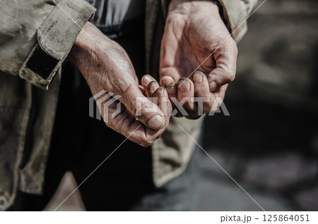 Wrinkled and covered in dirt, the hands tremble as they reach out, symbolizing desperation and struggle. The hands of a beggar ask for alms. 125864051