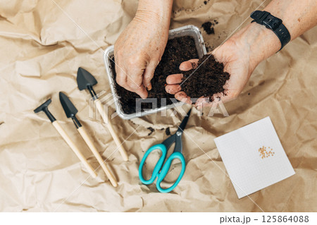 Kraft paper background, fertile soil and garden tools, top view. Hands planting seeds 125864088