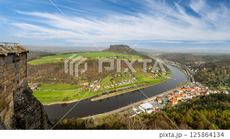 Overlooking the majestic Elbe River from Konigstein Fortress, visitors enjoy a breathtaking panorama of lush landscapes and quaint villages nestled along the riverbanks in Saxony, Germany. 125864134