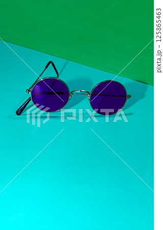 A pair of round purple sunglasses on a blue and green background 125865463