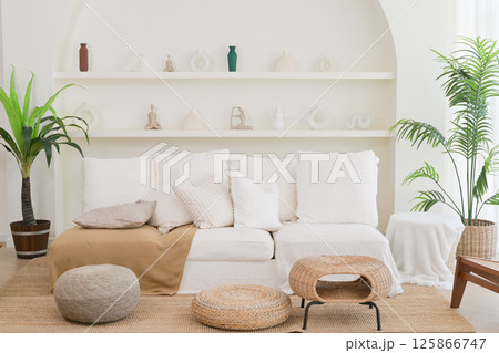 Cozy interior living room with white sofa, natural woven furniture, and green plants creating calm and inviting atmosphere 125866747