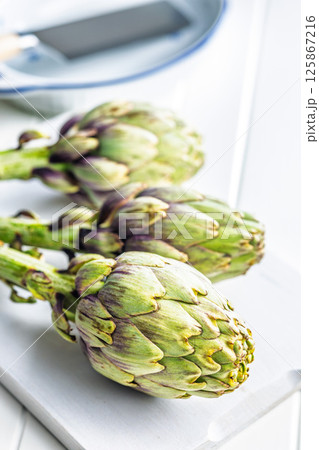 Ripe artichokes plant on white cutting board. 125867216