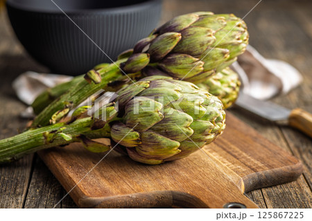 Ripe artichokes plant on cutting board on wooden table. 125867225