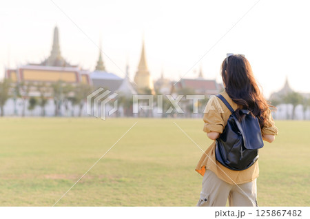 Southeast asian woman stands in large open field with backpack enjoying travel concept near historic temple buildings under bright daylight Southeast asian woman stands in large open field with backpack enjoying travel concept near historic temple buildings under bright daylight 125867482