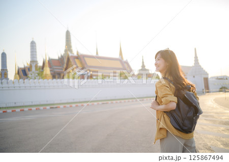 Southeast asian woman travel concept with backpack smiling near temple in bright sunlight for vacation and adventure Southeast asian woman travel concept with backpack smiling near temple in bright sunlight for vacation and adventure 125867494