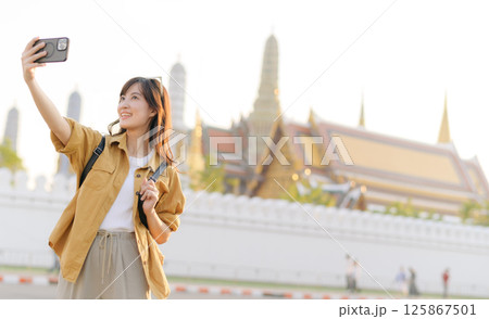 Southeast asian woman travel concept is captured as she joyfully takes selfie in front of historic temple, showcasing her excitement and cultural beauty of destination Southeast asian woman travel concept is captured as she joyfully takes selfie in front of historic temple, showcasing her excitement and cultural beauty of destination 125867501