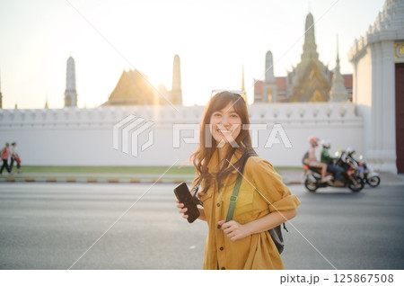 Southeast asian woman travel concept smiling with smartphone and backpack near temple in city during sunset light Southeast asian woman travel concept smiling with smartphone and backpack near temple in city during sunset light 125867508