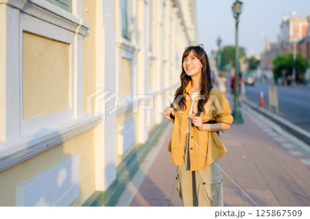 Southeast asian woman travel concept shows happy woman exploring city street with backpack and casual outfit enjoying her travel experience in warm sunlight Southeast asian woman travel concept shows happy woman exploring city street with backpack and casual outfit enjoying her travel experience in warm sunlight 125867509