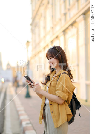 Southeast asian woman enjoys travel concept using her phone outdoors in warm light setting showing relaxed and happy mood Southeast asian woman enjoys travel concept using her phone outdoors in warm light setting showing relaxed and happy mood 125867517
