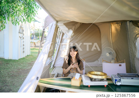 Southeast asian woman enjoys travel concept sitting inside tent smiling happily with phone in hand surrounded by camping equipment and nature outdoors Southeast asian woman enjoys travel concept sitting inside tent smiling happily with phone in hand surrounded by camping equipment and nature outdoors 125867556
