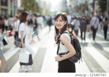 Southeast asian woman smiling with backpack walking on busy city street crosswalk in daylight Southeast asian woman smiling with backpack walking on busy city street crosswalk in daylight 125867587