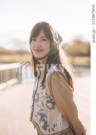 Southeast asian woman smiles gently while travel outdoors wearing floral vest and headscarf capturing peaceful travel concept in soft natural light 125867658
