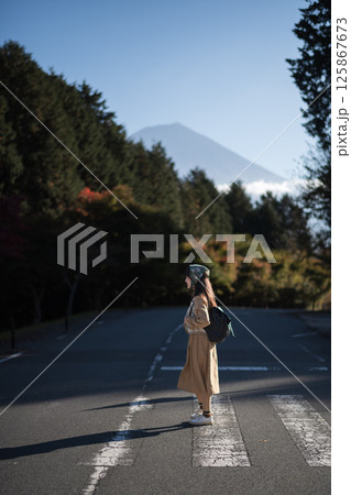 Southeast asian woman stands on quiet road surrounded by forest trees with mountain in background under clear blue sky creating peaceful and calm atmosphere Southeast asian woman stands on quiet road surrounded by forest trees with mountain in background under clear blue sky creating peaceful and calm atmosphere 125867673