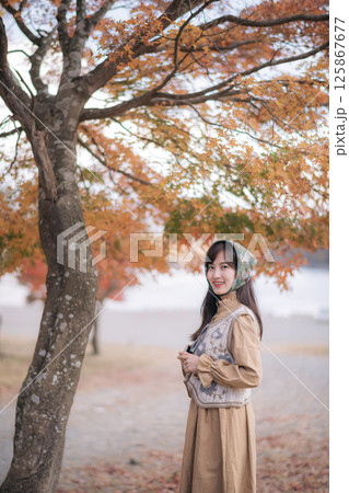Southeast asian woman enjoys travel concept in autumn park wearing vintage style dress and headscarf smiling under orange leaves tree with peaceful natural background Southeast asian woman enjoys travel concept in autumn park wearing vintage style dress and headscarf smiling under orange leaves tree with peaceful natural background 125867677