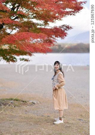 Southeast asian woman enjoys travel concept standing near lake with autumn red leaves above her creating peaceful and joyful outdoor scene in nature Southeast asian woman enjoys travel concept standing near lake with autumn red leaves above her creating peaceful and joyful outdoor scene in nature 125867690