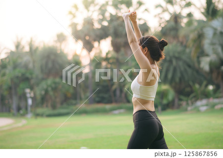 Southeast asian woman enjoying wellness and healthy lifestyle concept while doing exercise outdoors in green park, feeling relaxed and motivated in morning light Southeast asian woman enjoying wellness and healthy lifestyle concept while doing exercise outdoors in green park, feeling relaxed and motivated in morning light 125867856