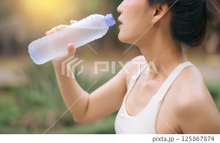 Southeast asian woman enjoying wellness and healthy lifestyle concept while exercising outdoors and drinking water for hydration and refreshment in natural environment 125867874