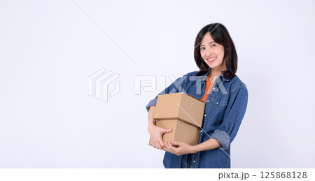 Southeast asian woman shopping online happily holds two cardboard boxes wearing casual denim shirt and orange top against white background in bright cheerful mood 125868128
