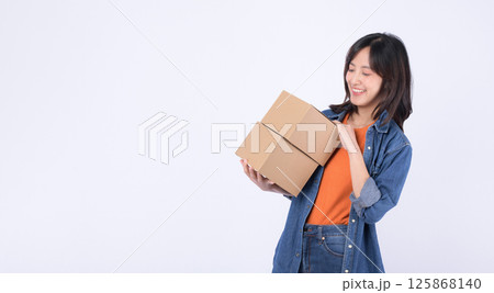 Southeast asian woman shopping online is happily holding two cardboard boxes wearing casual denim clothes and orange shirt against plain white background Southeast asian woman shopping online is happily holding two cardboard boxes wearing casual denim clothes and orange shirt against plain white background 125868140
