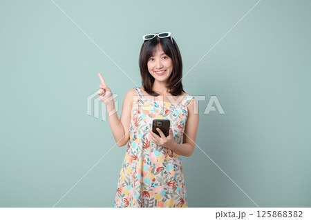 Southeast asian woman smiling happily while holding mobile phone and pointing up as if explaining internet application on pastel background Southeast asian woman smiling happily while holding mobile phone and pointing up as if explaining internet application on pastel background 125868382